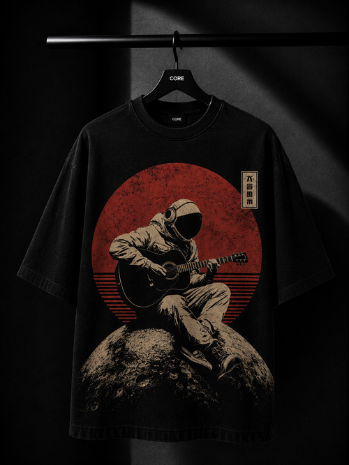 Black oversized T-shirt featuring a vintage-style astronaut playing an acoustic guitar while sitting on the moon, set against a distressed red retro sun graphic. Displayed on a premium hanger in a luxury dark studio setting.