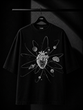 Premium black oversized T-shirt with a minimalist white botanical leaf print cascading from the right shoulder, displayed on a wooden hanger in a luxury studio setting.
