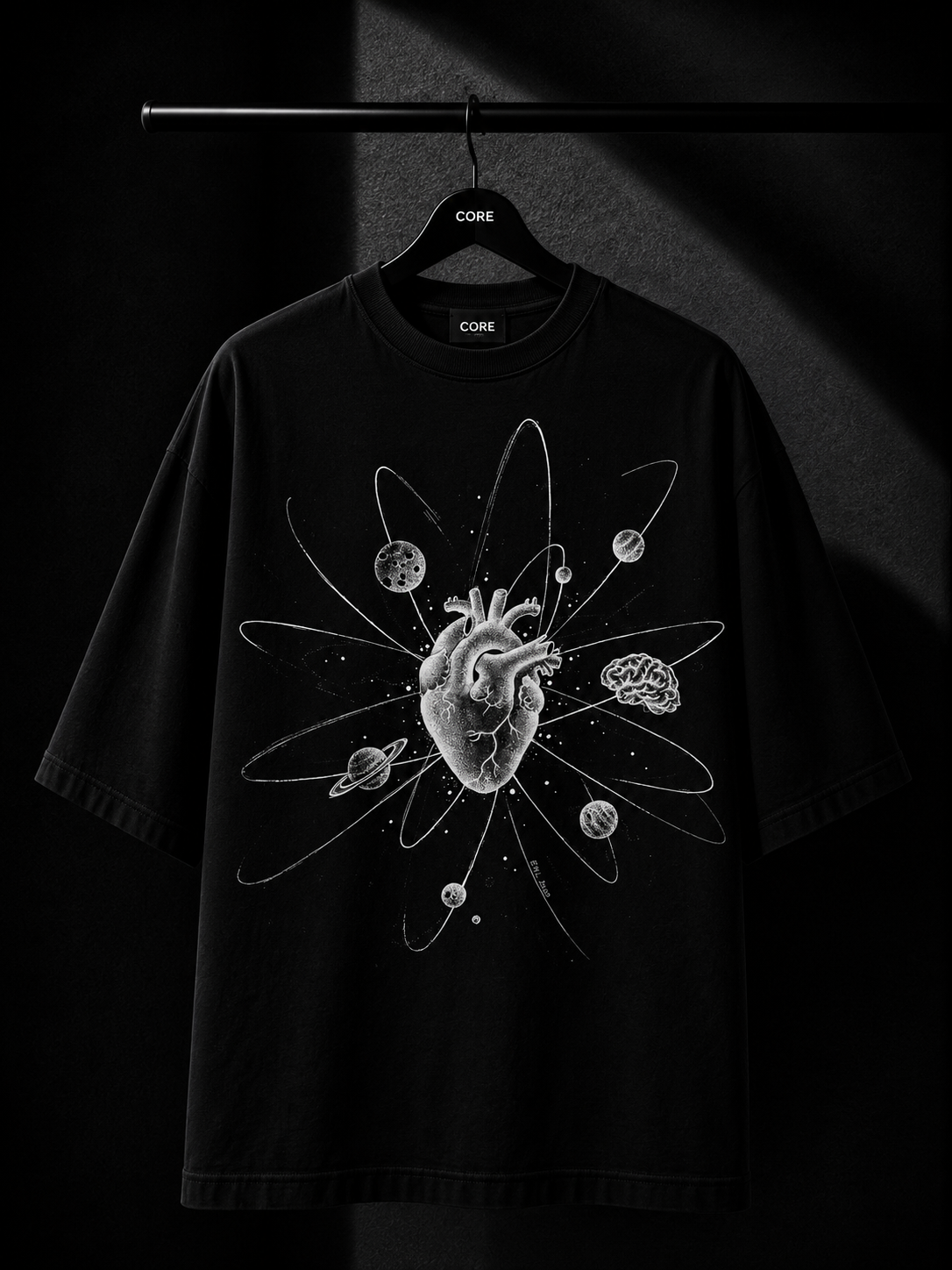 Premium black oversized T-shirt with a minimalist white botanical leaf print cascading from the right shoulder, displayed on a wooden hanger in a luxury studio setting.