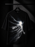 Black oversized T-shirt with a minimalist white cascading leaf graphic across the right shoulder, hanging on a premium wooden hanger in a luxury dark studio setting.
