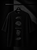 Black oversized T-shirt featuring a minimalist white leaf graphic cascading from the right shoulder onto the chest, displayed on a wooden hanger in a premium dark studio setting.