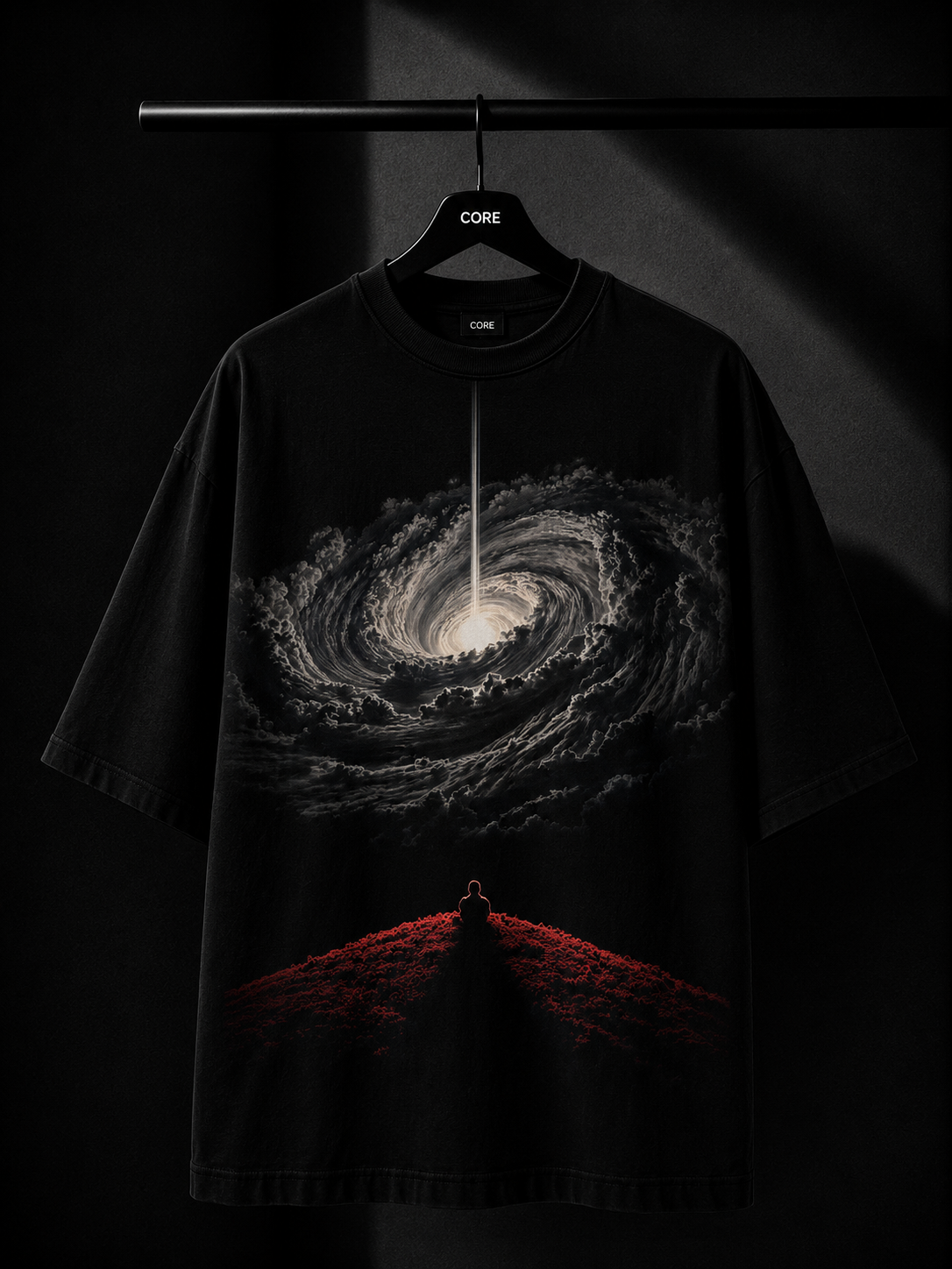 Black oversized T-shirt featuring a dramatic cosmic vortex graphic with a lone meditating silhouette on a red hill, displayed on a premium wooden hanger in a luxury dark studio setting.